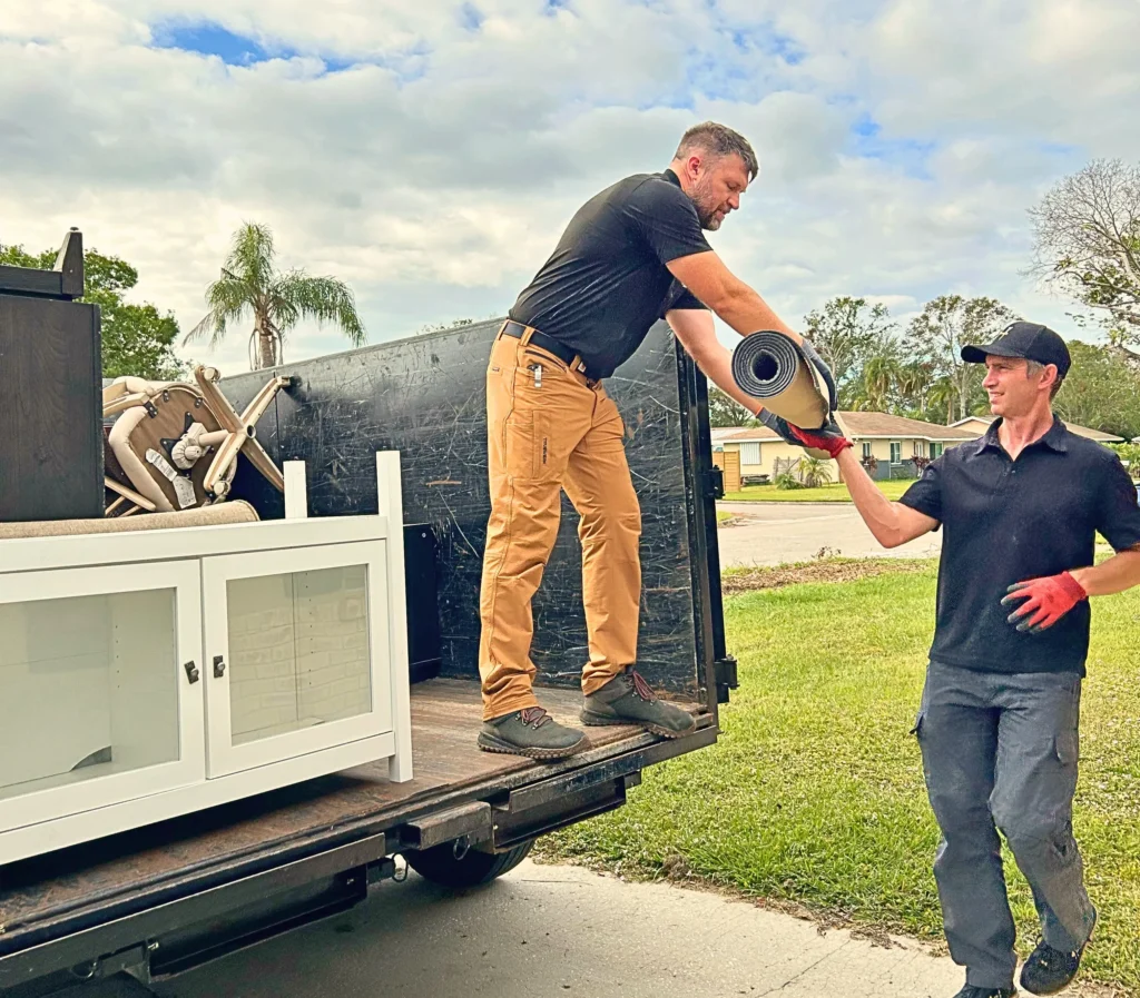 Manatee Junk Bros team members carefully loading a white cabinet and rug into a trailer during a residential furniture removal job in Bradenton.